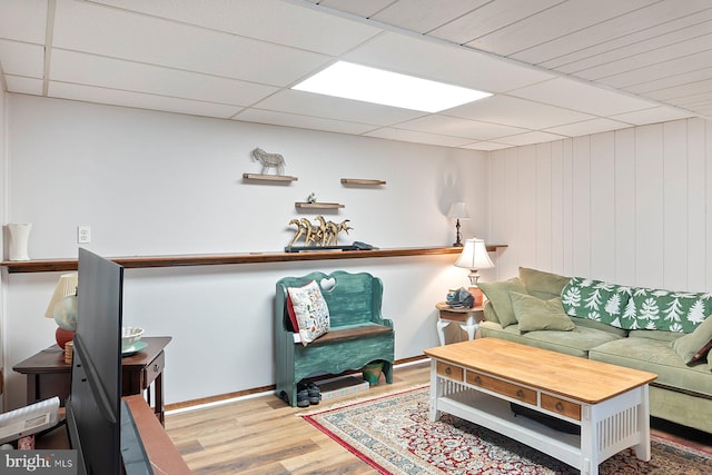 living area featuring a paneled ceiling, baseboards, and wood finished floors