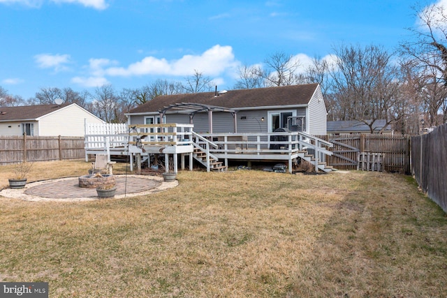 back of house featuring a deck, a fire pit, a lawn, and a fenced backyard