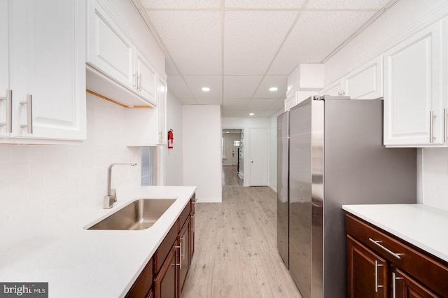 kitchen featuring light countertops, freestanding refrigerator, light wood-style floors, white cabinetry, and a sink