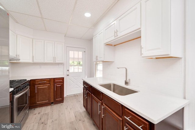 kitchen with gas range, white cabinetry, light countertops, and a sink