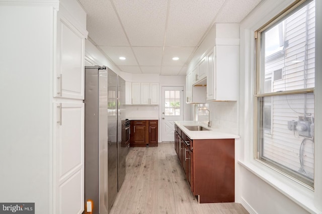 kitchen featuring light wood-style flooring, a sink, white cabinetry, light countertops, and decorative backsplash