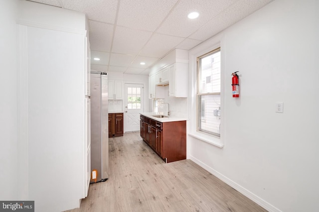 kitchen featuring light countertops, decorative backsplash, light wood-style flooring, freestanding refrigerator, and a sink