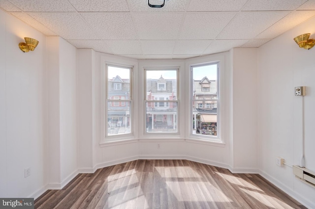 spare room with a baseboard heating unit, a paneled ceiling, baseboards, and wood finished floors