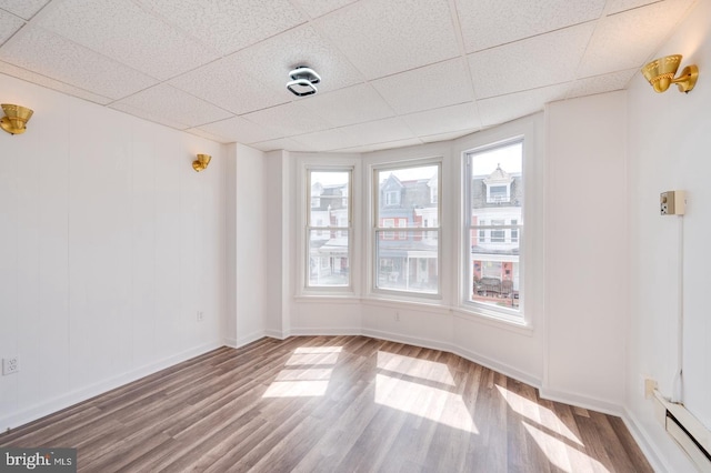 empty room with wood finished floors, baseboards, a drop ceiling, and a baseboard radiator