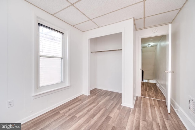 unfurnished bedroom featuring baseboards, wood finished floors, a closet, and a paneled ceiling