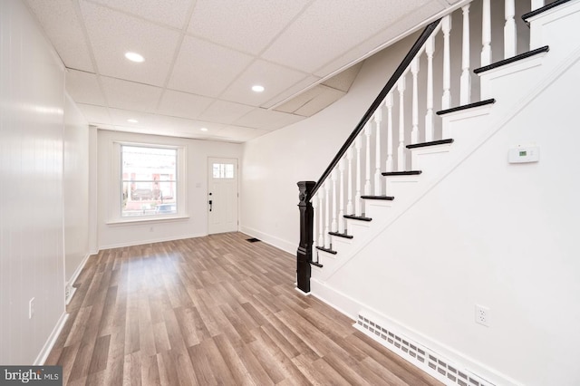 foyer entrance featuring visible vents, light wood-style flooring, a drop ceiling, stairway, and baseboards