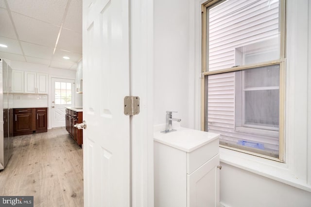 bathroom with two vanities, wood finished floors, a drop ceiling, and a sink