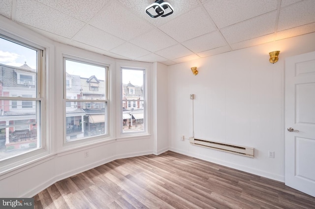 unfurnished room with wood finished floors, a paneled ceiling, baseboards, and a baseboard radiator