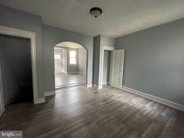 interior space with baseboards, arched walkways, and wood finished floors