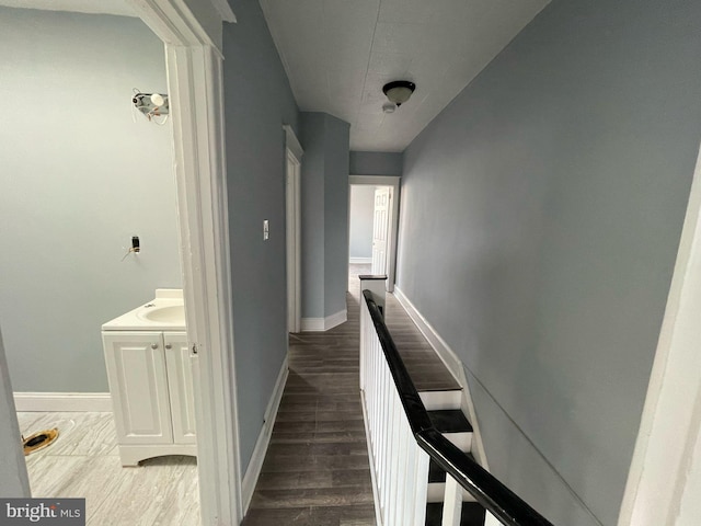 hall with a sink, baseboards, an upstairs landing, and wood finished floors