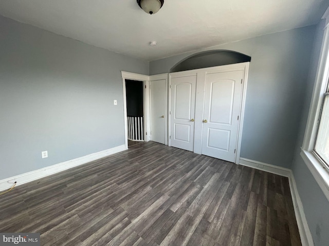 unfurnished bedroom featuring a closet, baseboards, and dark wood-style flooring