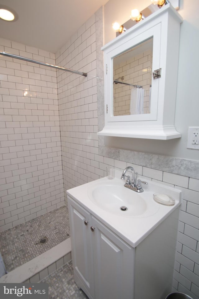 full bath with a tile shower, tile walls, and vanity