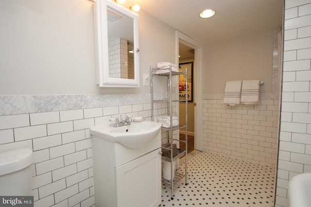 full bath with vanity, tiled shower, tile patterned flooring, wainscoting, and tile walls