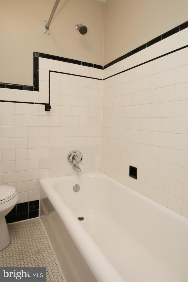 bathroom with tile patterned flooring, tile walls, toilet, and a tub