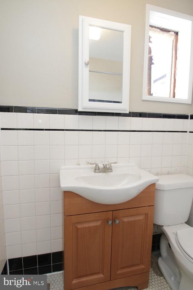 half bathroom featuring tile patterned floors, a wainscoted wall, toilet, tile walls, and vanity