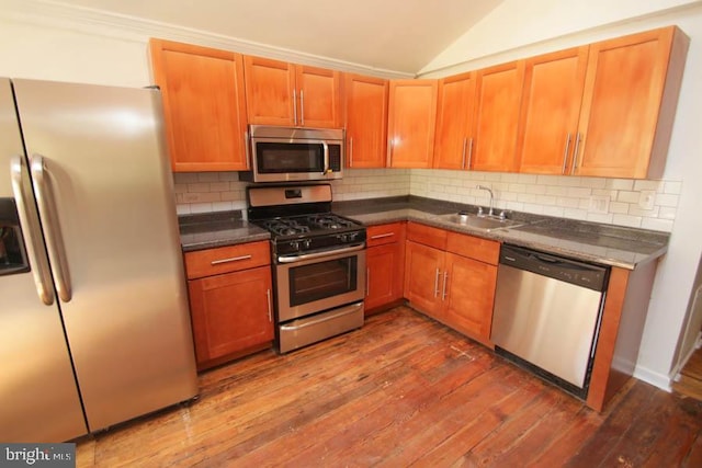 kitchen featuring dark countertops, dark wood-type flooring, vaulted ceiling, appliances with stainless steel finishes, and a sink