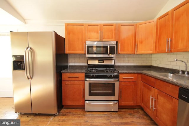 kitchen with backsplash, wood finished floors, appliances with stainless steel finishes, and a sink