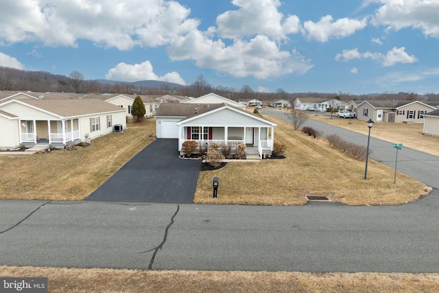 view of front of home featuring driveway, covered porch, a residential view, and a front lawn