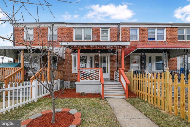 view of property featuring brick siding, a porch, and fence