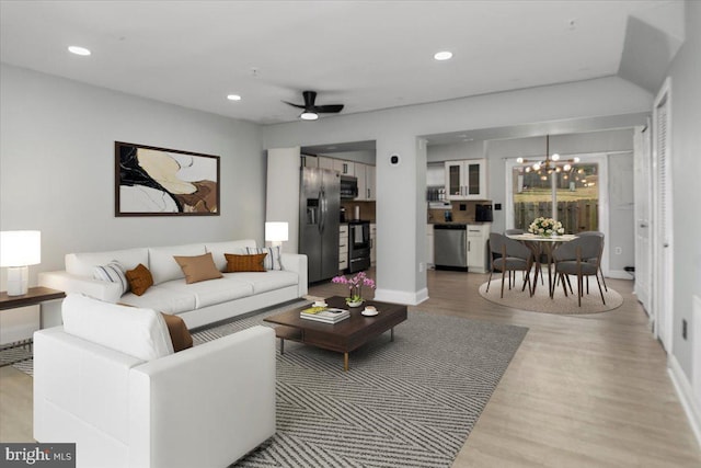 living area with ceiling fan with notable chandelier, baseboards, light wood-style flooring, and recessed lighting