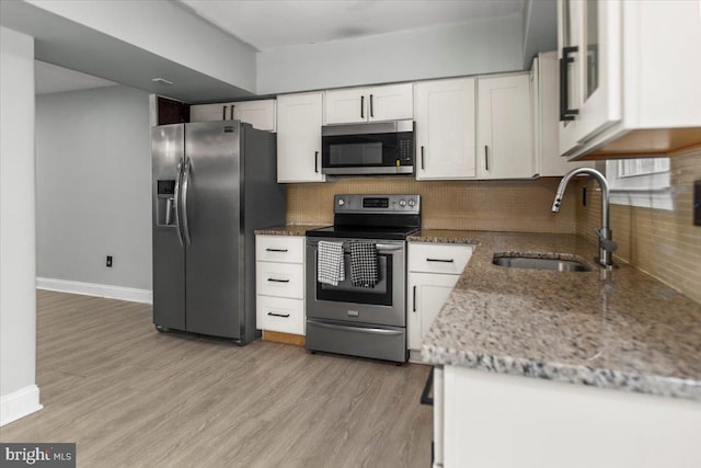 kitchen with decorative backsplash, stainless steel appliances, light wood-style floors, white cabinetry, and a sink