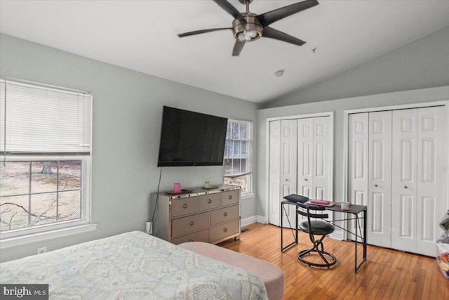 bedroom with hardwood / wood-style flooring, a ceiling fan, baseboards, vaulted ceiling, and multiple closets