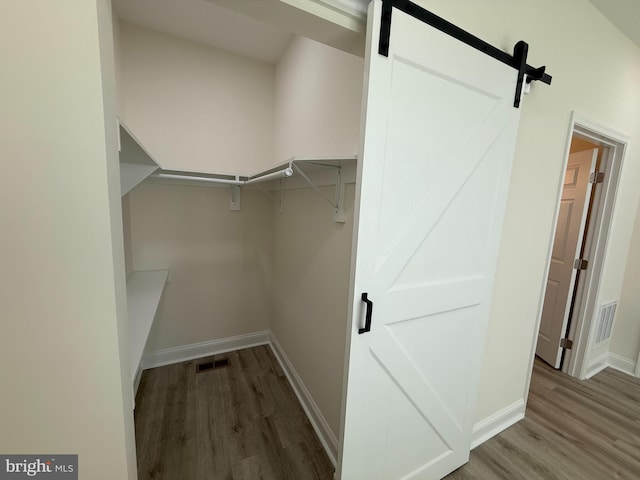 walk in closet with visible vents, a barn door, and wood finished floors