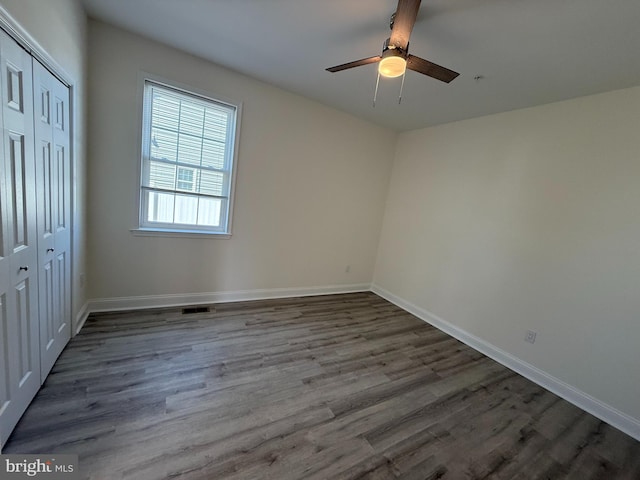 unfurnished bedroom with a ceiling fan, visible vents, wood finished floors, baseboards, and a closet