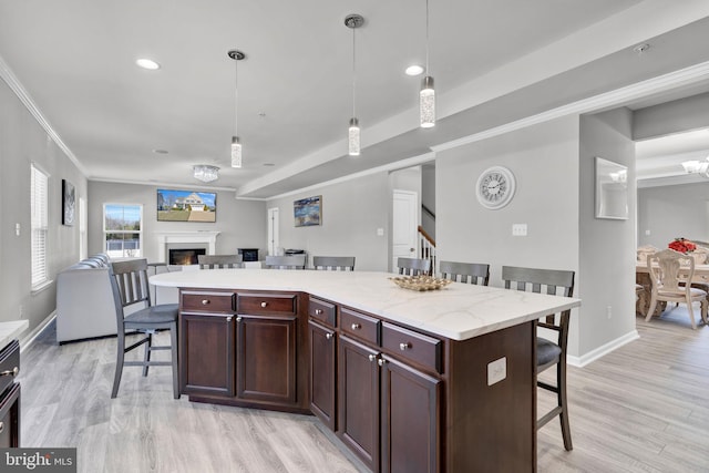 kitchen featuring a breakfast bar, open floor plan, a glass covered fireplace, crown molding, and light wood finished floors