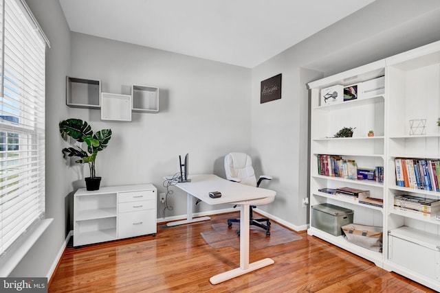 office area with a wall mounted air conditioner, light wood-type flooring, and baseboards