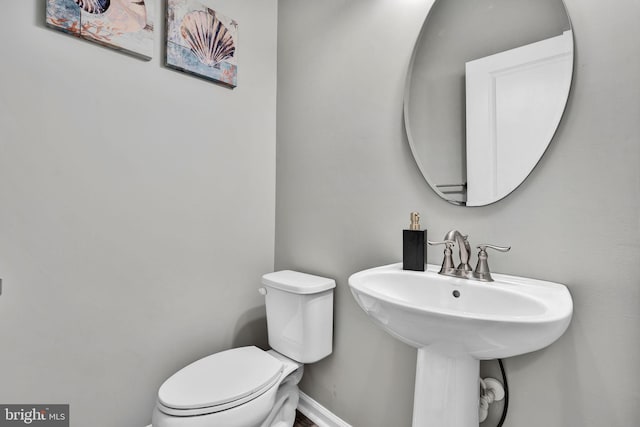 half bathroom with toilet, baseboards, and a sink