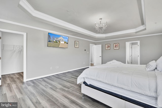 bedroom featuring wood finished floors, baseboards, an inviting chandelier, a walk in closet, and a raised ceiling