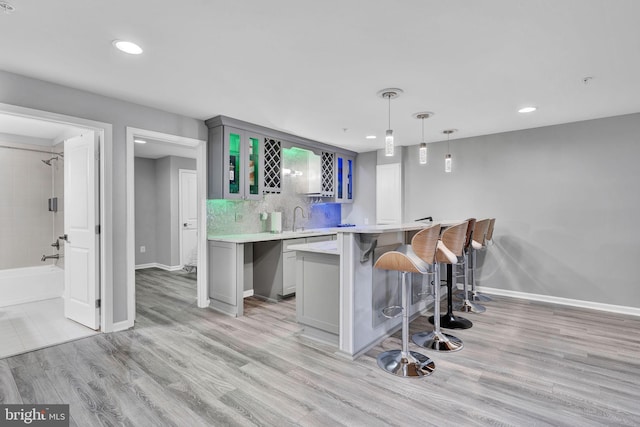 bar with backsplash, baseboards, pendant lighting, light wood-type flooring, and wet bar