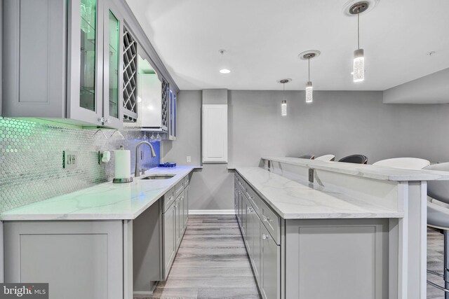 kitchen featuring backsplash, a kitchen bar, gray cabinets, a peninsula, and a sink