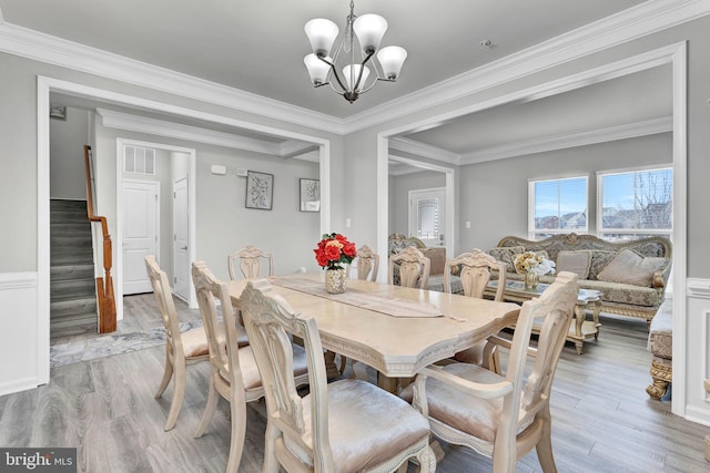 dining area with stairway, visible vents, an inviting chandelier, ornamental molding, and light wood-type flooring