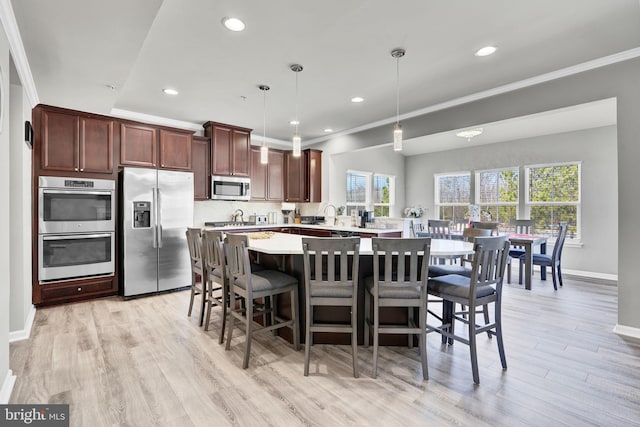 kitchen with plenty of natural light, ornamental molding, light countertops, appliances with stainless steel finishes, and light wood-type flooring