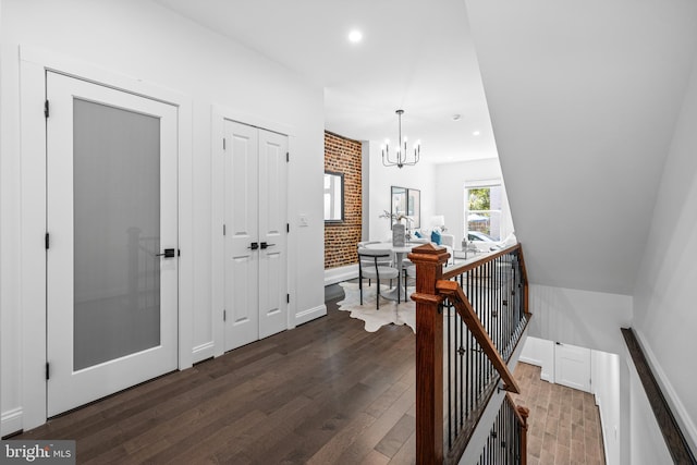 hall featuring dark wood-style floors, brick wall, an inviting chandelier, an upstairs landing, and recessed lighting