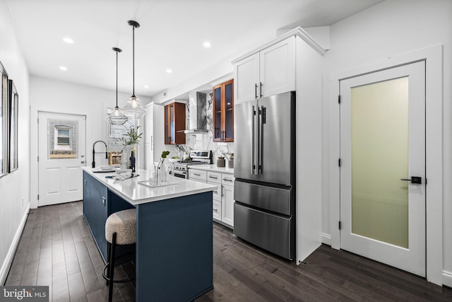 kitchen with premium appliances, light countertops, dark wood-type flooring, a kitchen island with sink, and wall chimney range hood