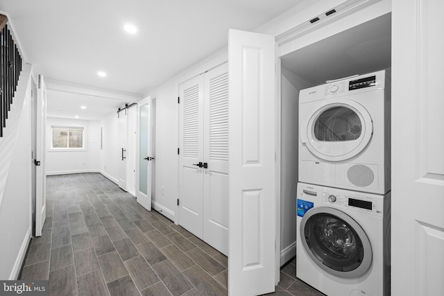 laundry area featuring laundry area, a barn door, baseboards, and stacked washer and dryer