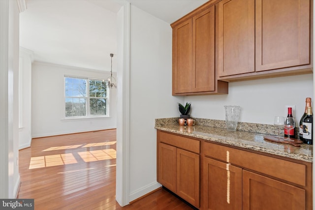 kitchen featuring hardwood / wood-style floors, light stone counters, brown cabinetry, and baseboards