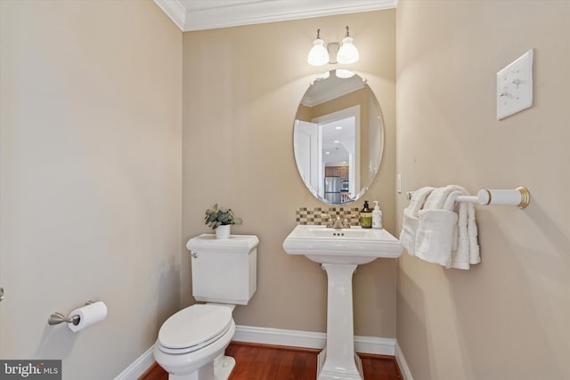 half bathroom with wood finished floors, baseboards, crown molding, toilet, and backsplash