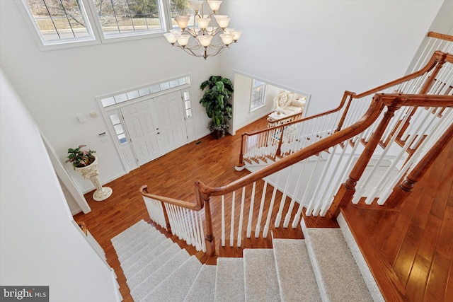 foyer entrance with stairs, an inviting chandelier, a high ceiling, and wood finished floors