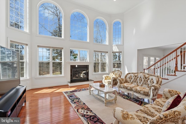 living area with a healthy amount of sunlight, stairway, ornamental molding, a glass covered fireplace, and wood-type flooring