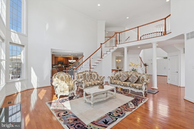 living room with baseboards, ornate columns, light wood-style flooring, stairs, and a towering ceiling