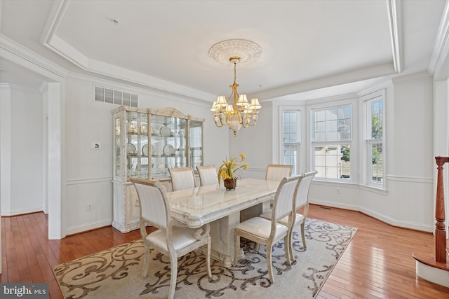 dining space with visible vents, ornamental molding, hardwood / wood-style flooring, a tray ceiling, and an inviting chandelier