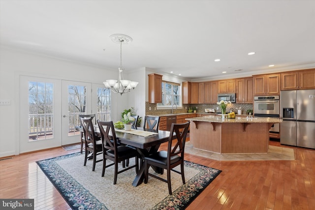 dining space with light wood-style flooring, recessed lighting, an inviting chandelier, crown molding, and baseboards