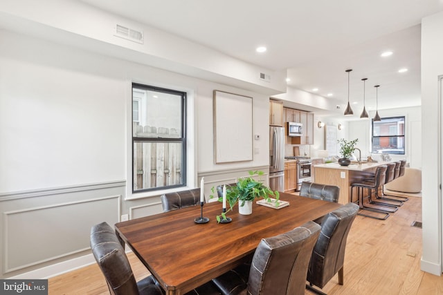 dining room featuring a decorative wall, recessed lighting, visible vents, and light wood-style floors