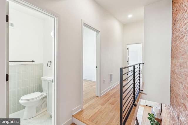 corridor with brick wall, light wood finished floors, visible vents, and tile walls