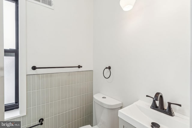 half bath featuring visible vents, a sink, toilet, and tile walls