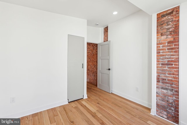 unfurnished bedroom with light wood-style floors, brick wall, baseboards, and recessed lighting